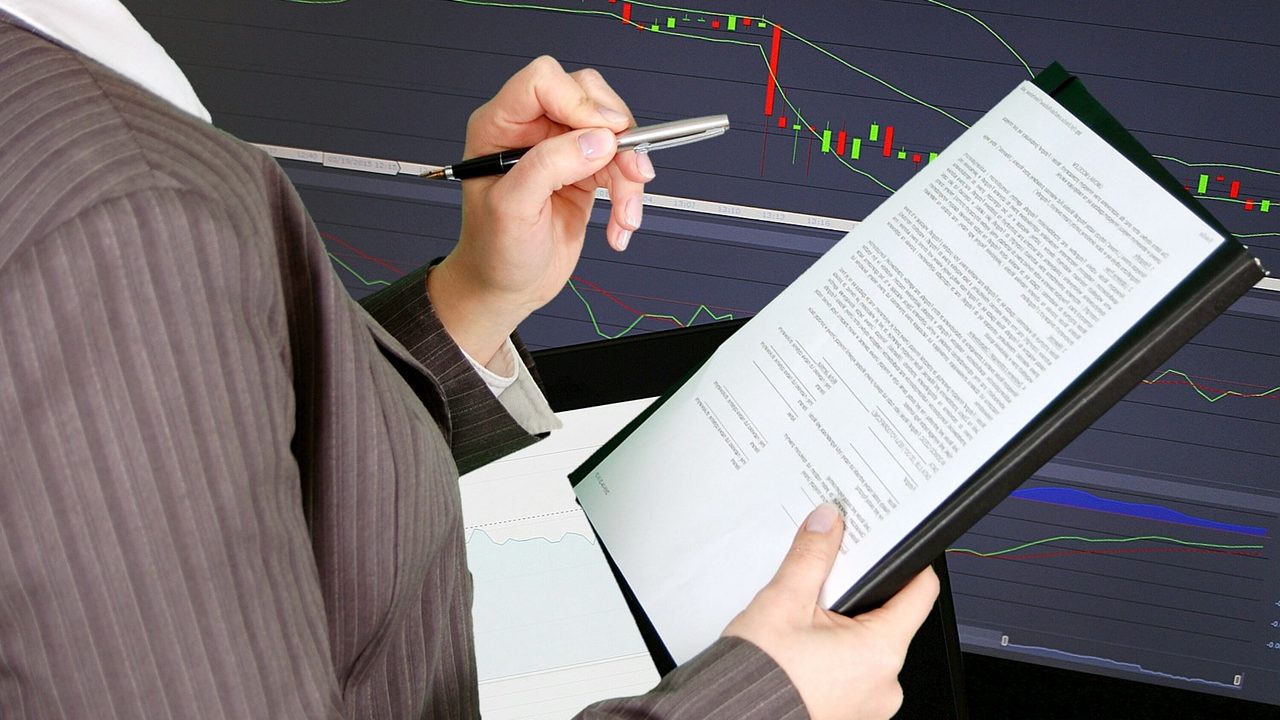 Imagem mostra gráfico e uma investidora calculando o preço alvo das ações